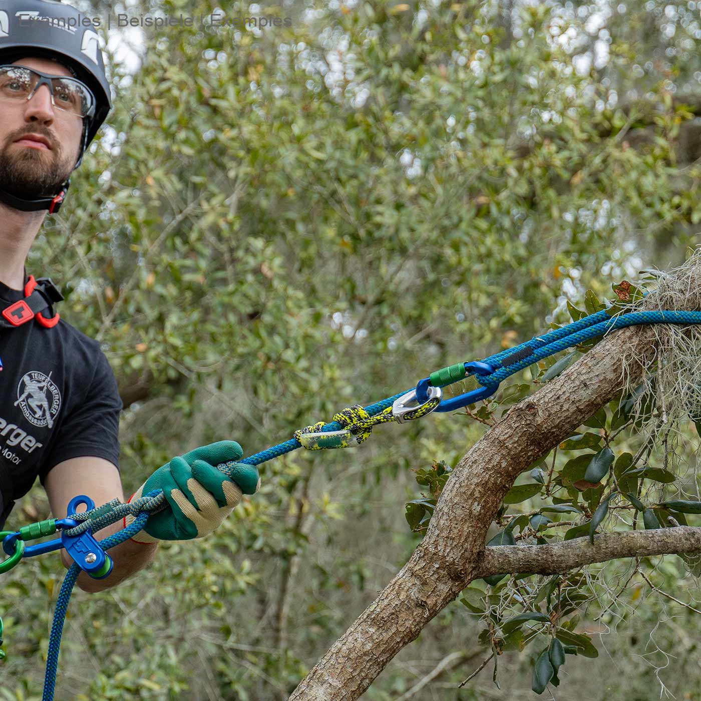 Man in helmet and gloves pulling blue rope hipSTAR Glide 11.5 attached to a tree branch surrounded by greenery