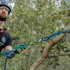 Man in helmet and gloves pulling blue rope hipSTAR Glide 11.5 attached to a tree branch surrounded by greenery