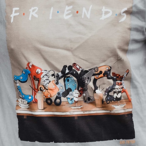 Close-up of the T-shirt print with the words "Friends" and detailed mechanical parts in different colors on a table, with the lettering "ARB FICTION" visible at the bottom right