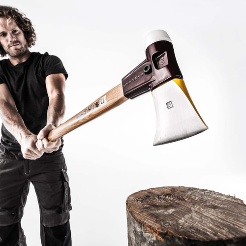 Man in black t-shirt holding the Simplex 750 axe over a wooden trunk, ready to strike