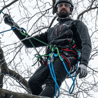 Man wearing the treeMOTION Pro X climbing harness with several blue and green ropes, black clothing, helmet and goggles in a tree, manufacturer Trufilanger