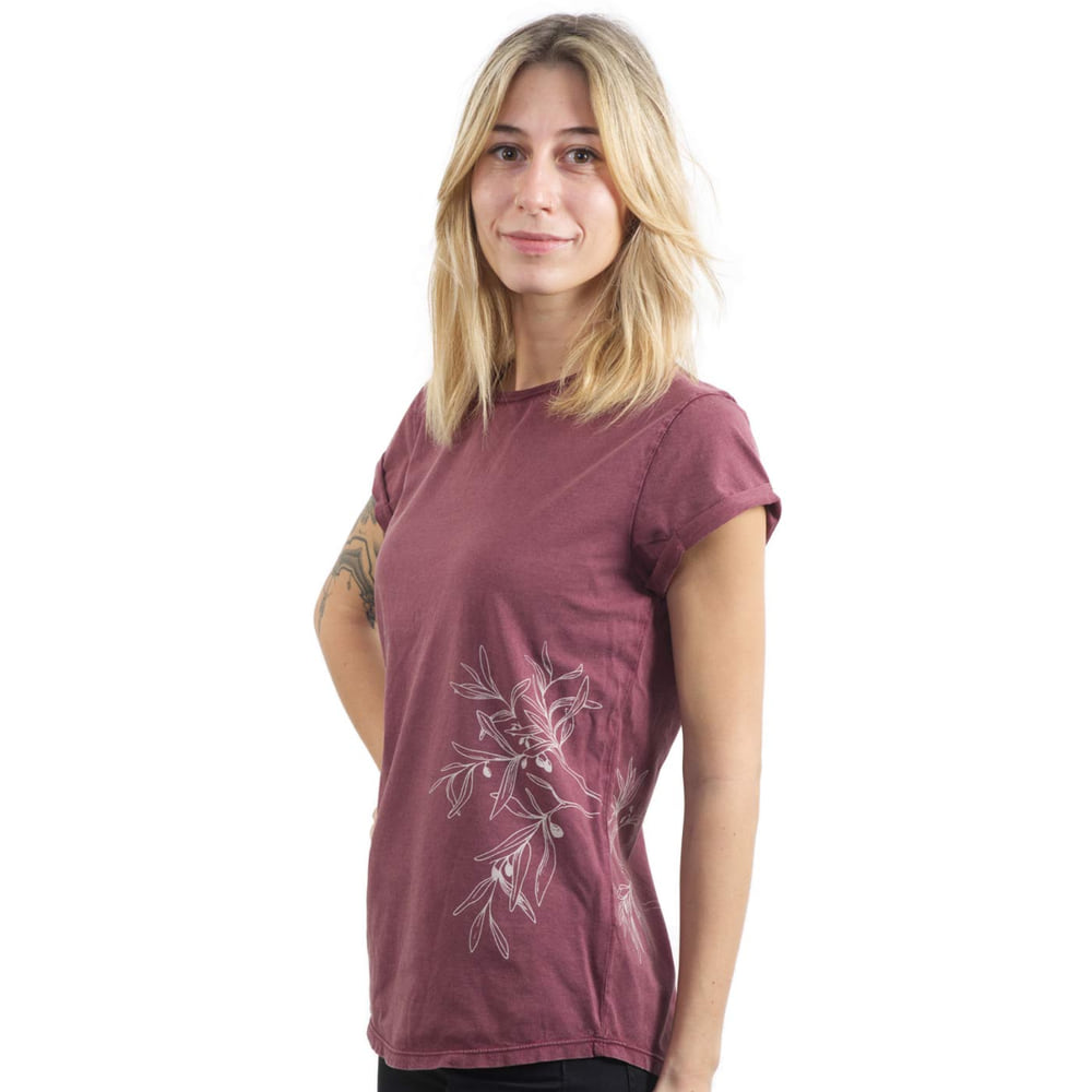 A woman wears a burgundy T-shirt "Olive Branch" with a white olive branch motif on the side and has her hands behind her back.