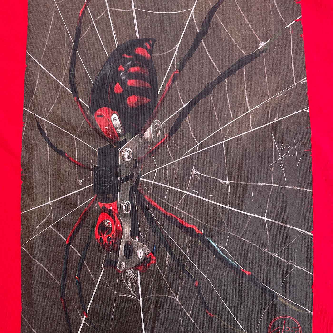 Close-up of spider print on the red ART Spider shirt, the spider has black and red colors and sits on a white spider web on a dark background