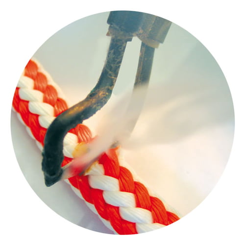 Close-up of a hot cutter heating and cutting a red and white braided string, with visible steam or smoke