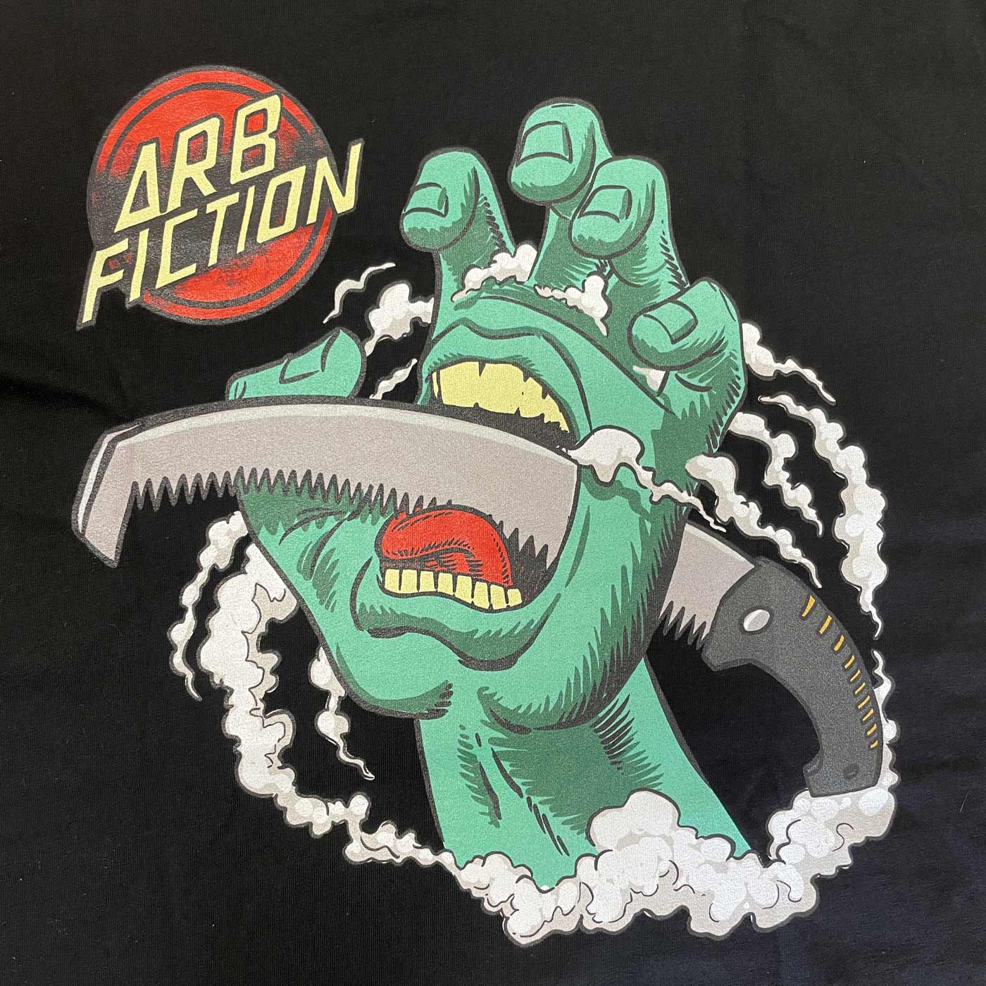 Close-up of the print on the black t-shirt with green hand, saw and red "ARB FICTION" logo, product name Screaming Hand
