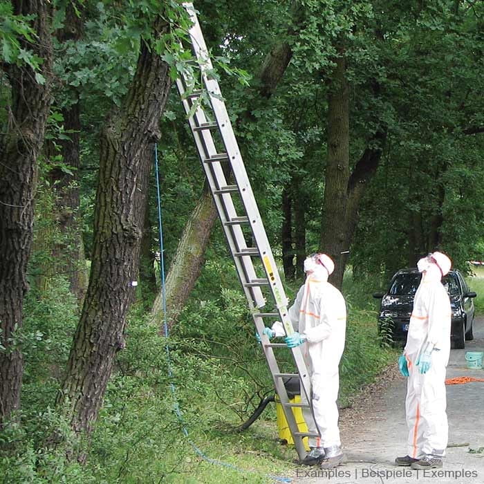 Two people in white EPS Guard protective suits with orange stripes, blue gloves and protective masks are standing next to a ladder in the forest, trees and a car can be seen in the background