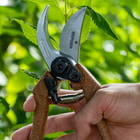 Berger C1200 secateurs with brown handles and silver blade, Berger brand, model C1200, held by one hand in front of green foliage