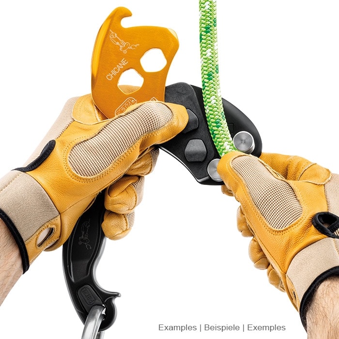 Petzl Chicane, yellow and black belay device with handle, held by two hands with yellow gloves on a green rope