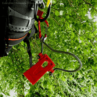 Arborist Micro Wedge by Arbpro, Red Plastic Wedge Tool with Green Rope and Red Carabiner, Hanging on Black Harness Against Green Foliage Background