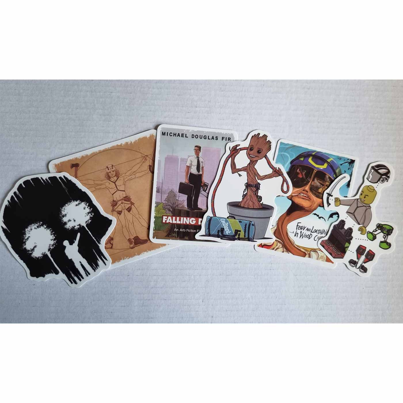 Six ARB Fiction Pack Vol. 3 stickers lie side by side on a white background, including a black sticker with two white trees, a sticker with a man in a suit and chainsaw that reads "Michael Douglas Fir Falling Down", a dancing tree in a flower pot, a man w