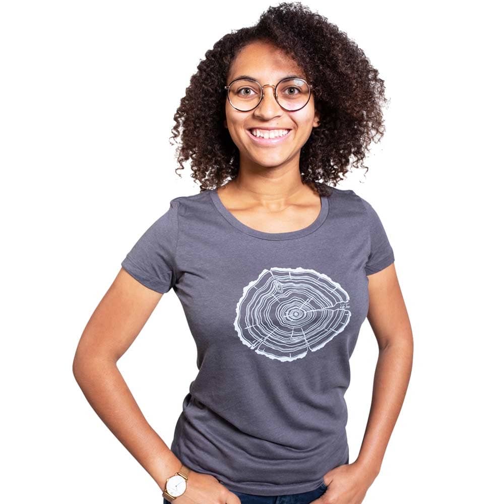 A woman with curly dark hair and glasses wears a gray Treeslice Women T-shirt with white tree trunk cut design on the front