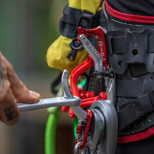 Close-up of a hand operating the Mega Vault carabiner in silver and red on a black and red strap