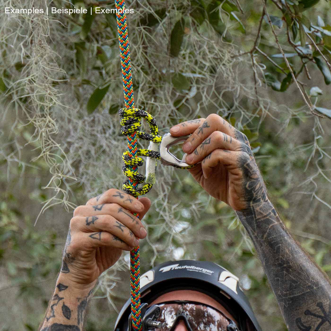 prusikLOOP fimble, a climbing rope with a silver metal part, held by the tattooed hands of a person with a helmet, in a forest environment