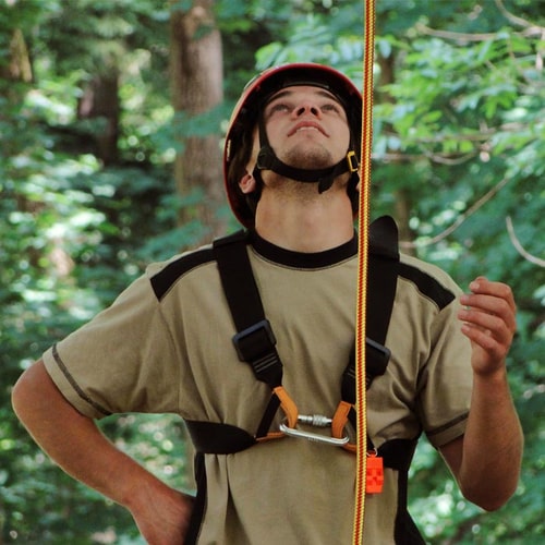 A man wears a red helmet and a climbing harness to which a red and yellow braided rope is attached, product name XP-e Highlight