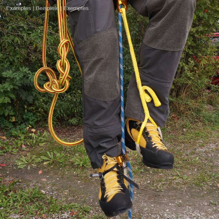 Bungee tool in blue with elastic, wavy section and flat webbing with black trim and green inner stripe on grey outdoor pants with yellow and black mountaineering boots and several climbing ropes