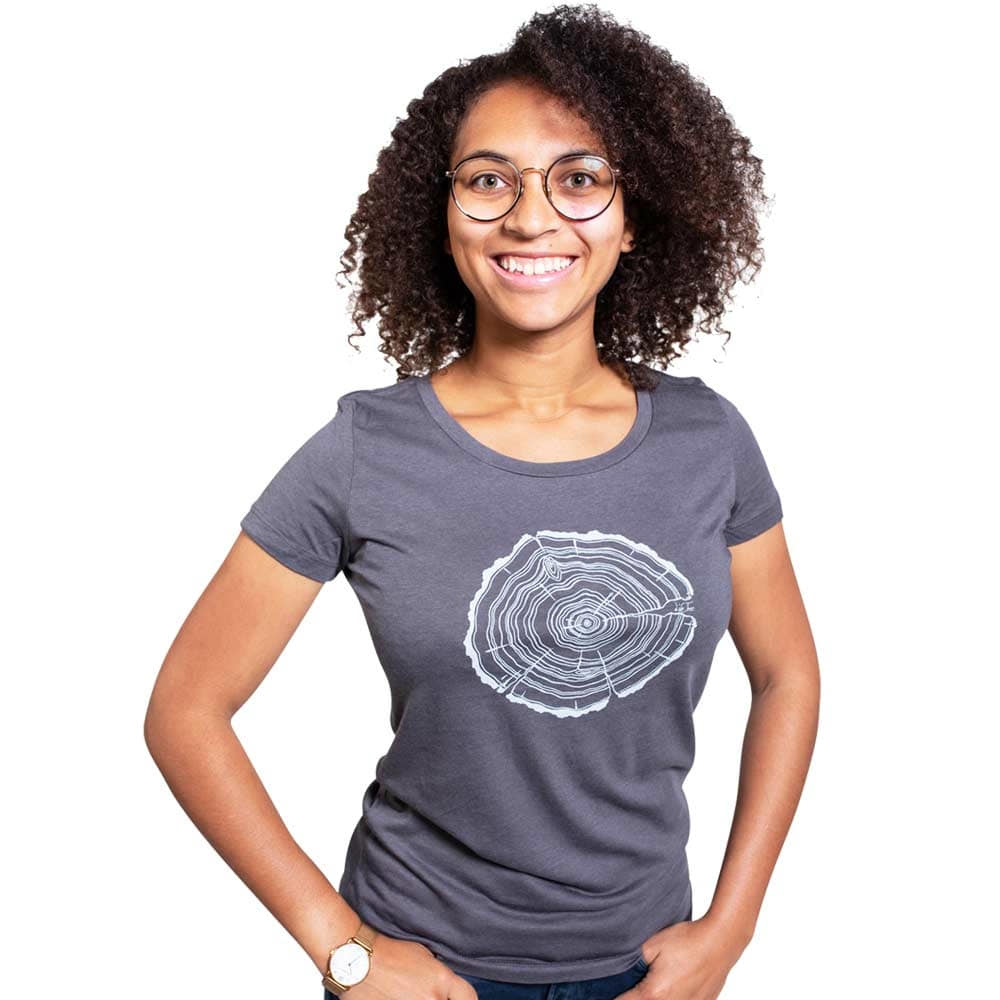 A woman with curly dark hair and glasses wears a gray Treeslice Women T-shirt with white tree trunk cut design on the front