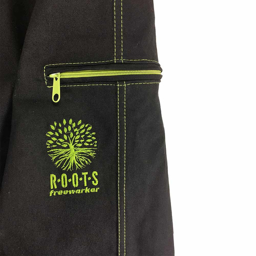 Close-up of a pocket of the Roots Pure outdoor pants in black with green zipper and green stitching, green embroidery of a tree with lettering "ROOTS freeworker"