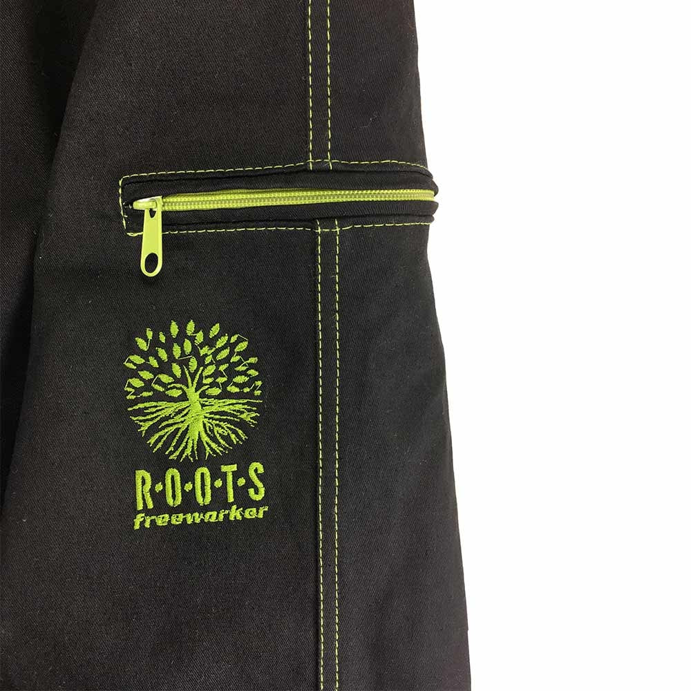Close-up of a pocket of the Roots Pure outdoor pants in black with green zipper and green stitching, green embroidery of a tree with lettering "ROOTS freeworker"