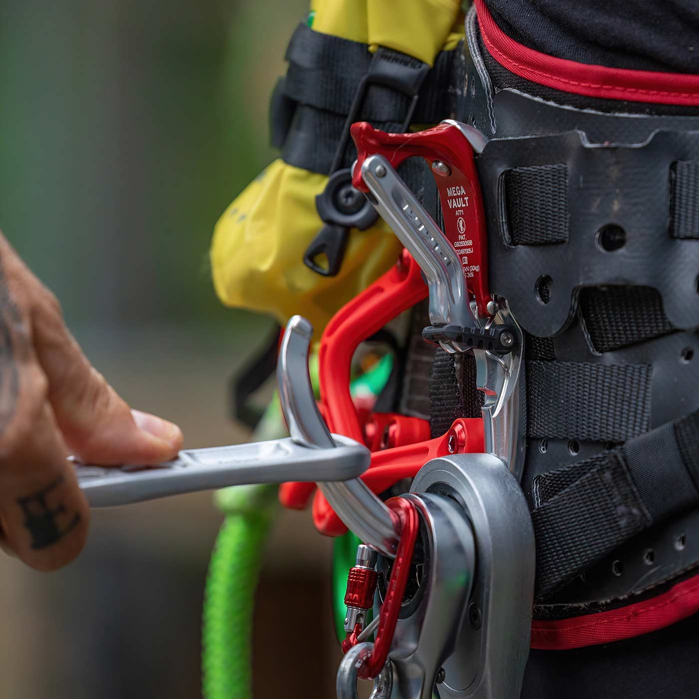 Close-up of a hand operating the Mega Vault carabiner in silver and red on a black and red strap