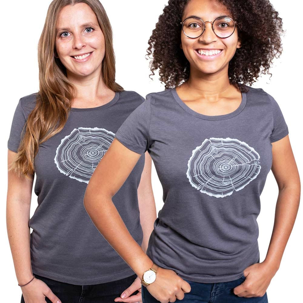 Two women are wearing gray Treeslice Women T-shirts with white tree trunk cut design on the front, one woman has long blonde hair, the other is wearing glasses and has curly dark hair