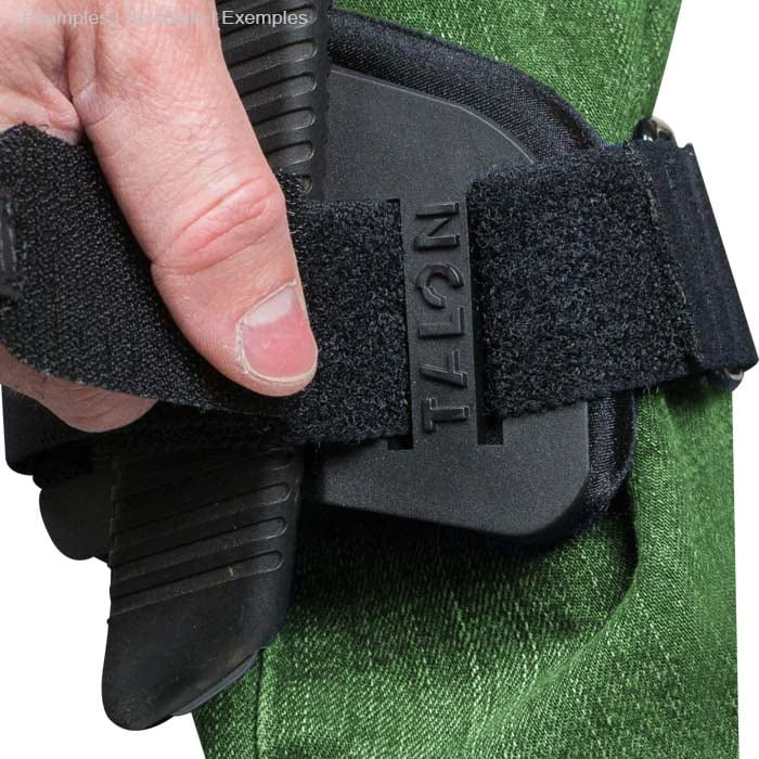 Close-up of a hand loosening the Velcro strap of the Talon Mount on green pants, black handsaw is attached in the holder