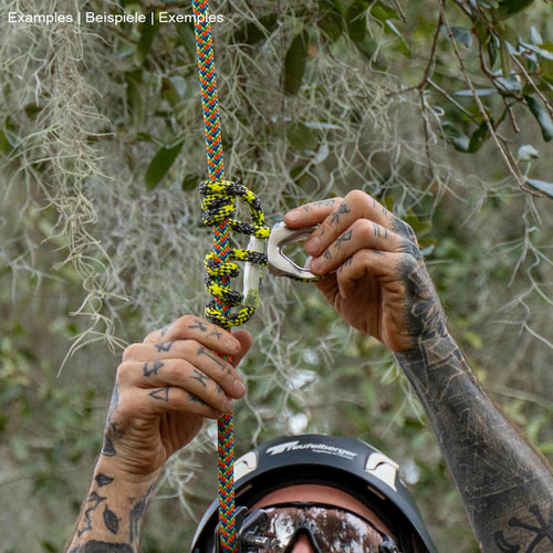 prusikLOOP fimble, a climbing rope with a silver metal part, held by the tattooed hands of a person with a helmet, in a forest environment
