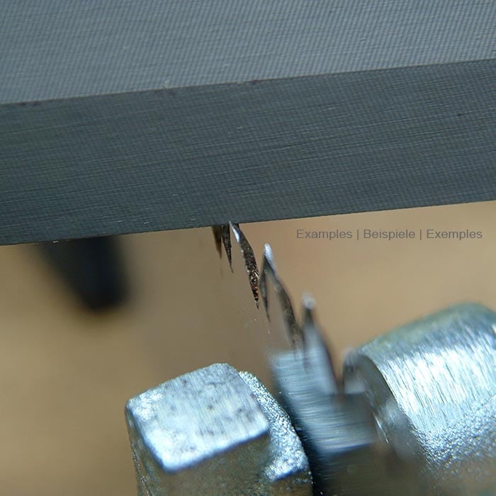 Close-up of a gray file being sharpened on the edge of a metal surface