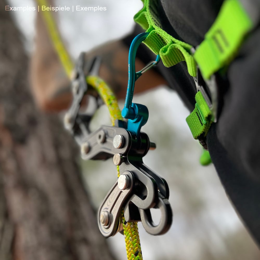Person wearing a green harness with a blue Magneato carabiner attached to it, connected to a black climbing frame and yellow rope, outdoors on a tree.