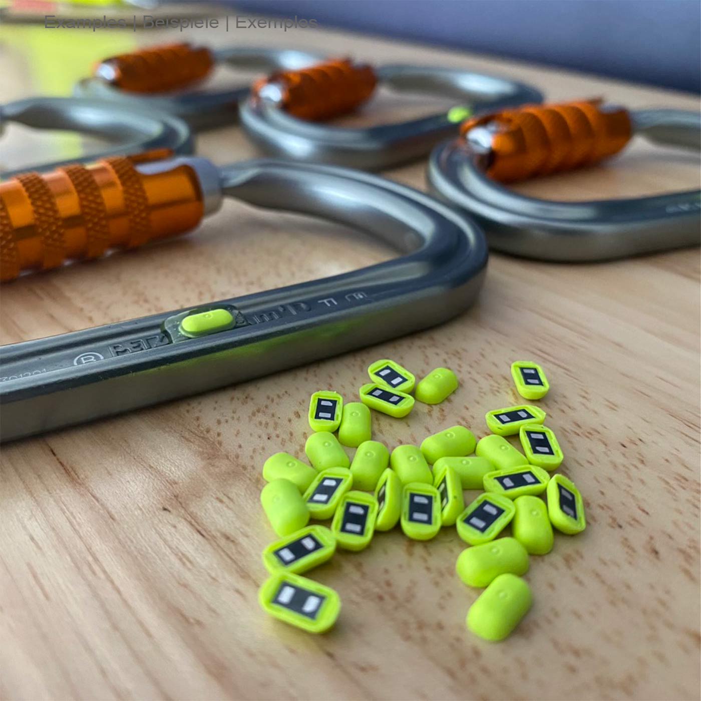 Hardware NFC Tag from Scannable, many small yellow-green NFC tags lie on a wooden table in front of several carabiners with orange closure