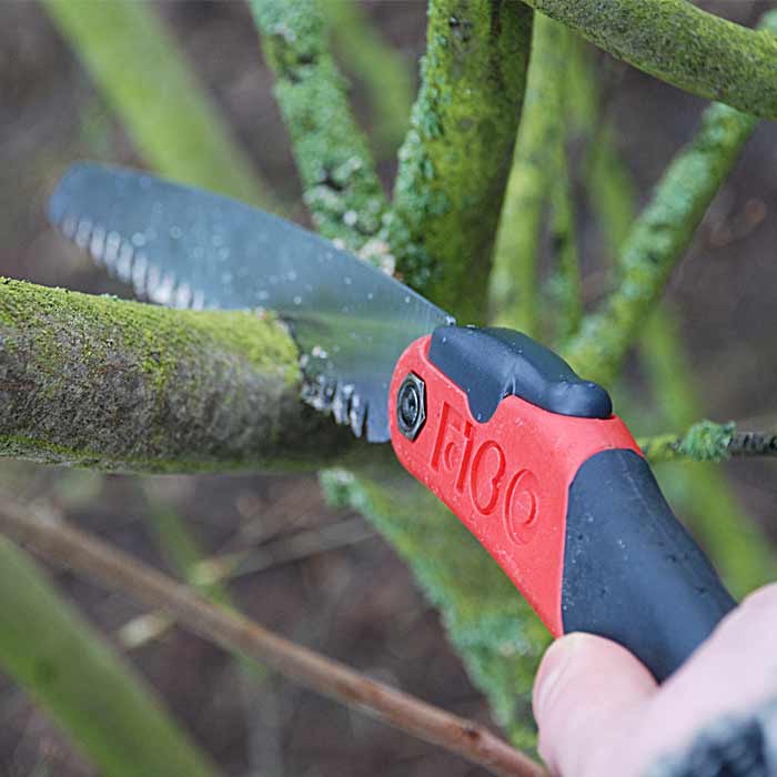 F180-7.5 Folding saw from FiGO with red and black handle, used for cutting a green branch, saw blade folded out