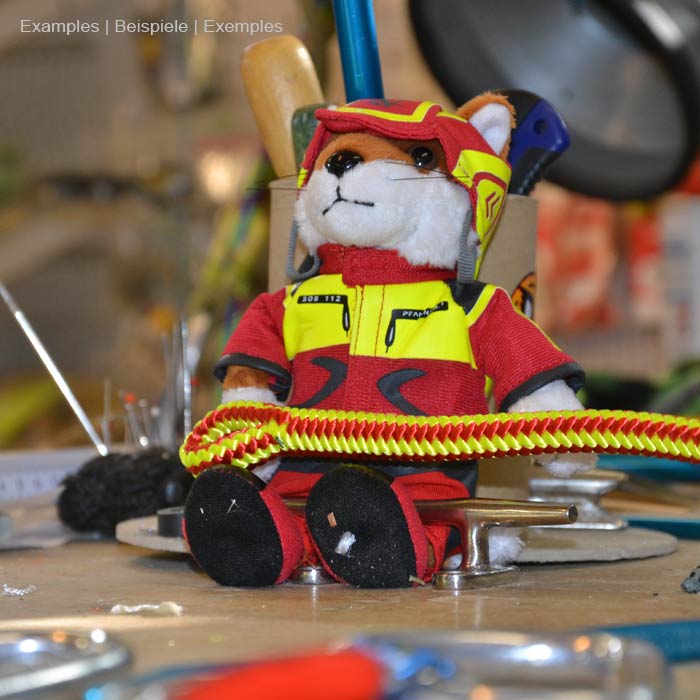 Wiffzack plush figure sitting on a table surrounded by tools, wearing red and yellow clothes and helmet