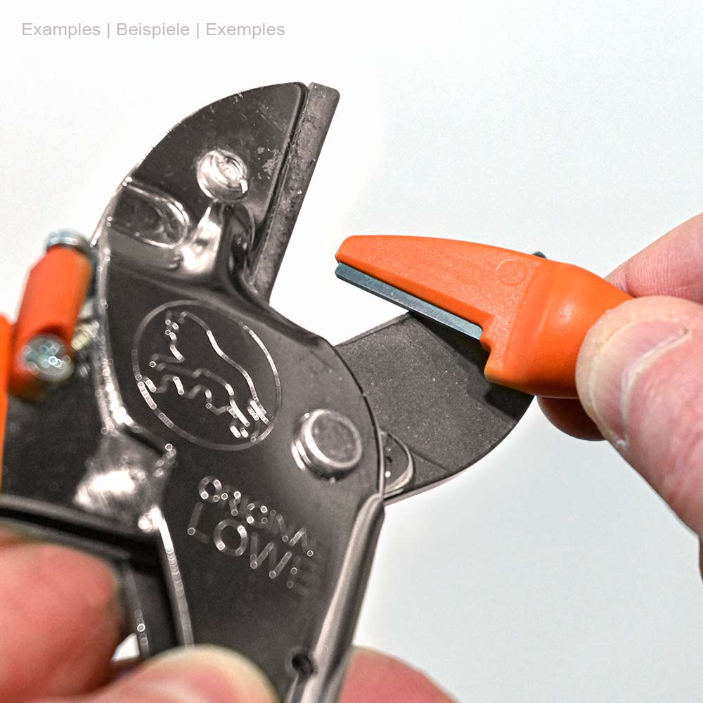 Hand holds the orange blade sharpener Original LÖWE and uses it to sharpen a black secateurs with the LÖWE logo