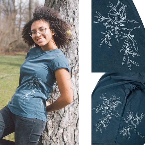 A woman leans against a tree and wears a dark blue T-shirt "Olive Branch" with a white olive branch motif, next to two close-ups of the print.