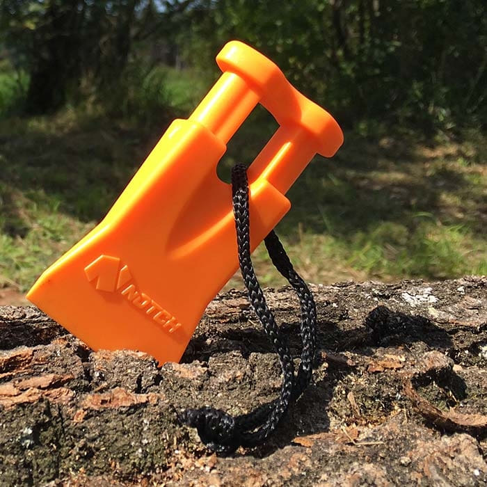 Climbers Best Friend Wedge by Notch, Orange Plastic Wedge with Black Cord Lies Diagonally on Tree Bark Outdoors